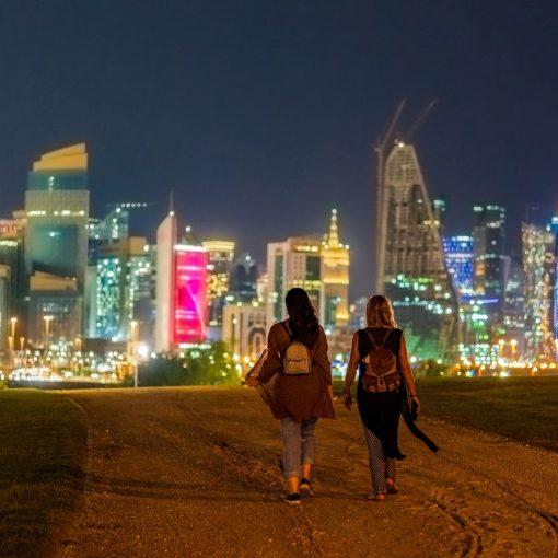 anonymous women walking in city near illuminated skyscrapers at night