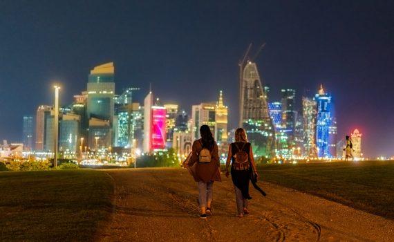 anonymous women walking in city near illuminated skyscrapers at night