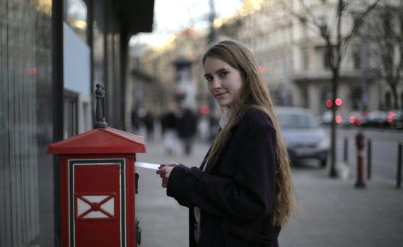 woman wearing violet coat while standing near mailbox