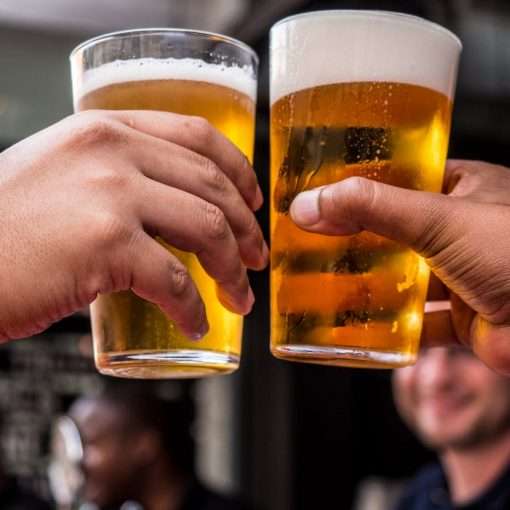 two persons holding drinking glasses filled with beer