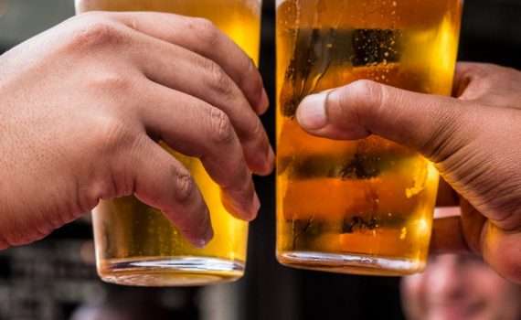 two persons holding drinking glasses filled with beer