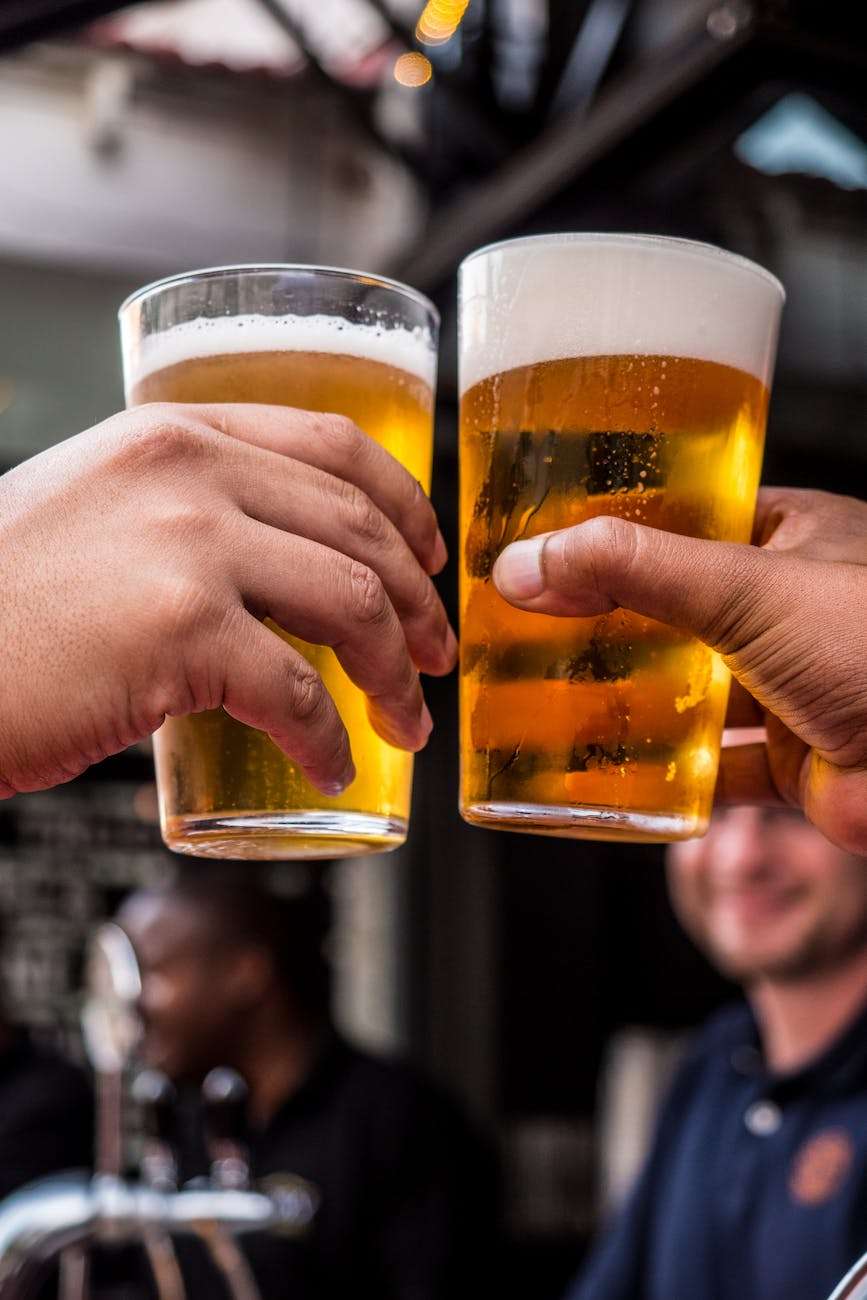 two persons holding drinking glasses filled with beer