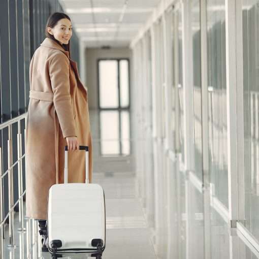 stylish happy traveler with suitcase in airport hallway