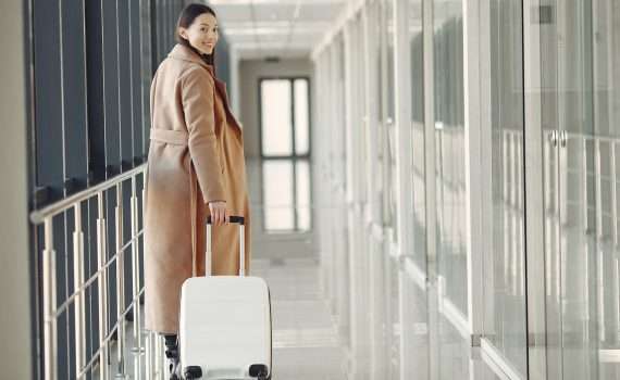 stylish happy traveler with suitcase in airport hallway