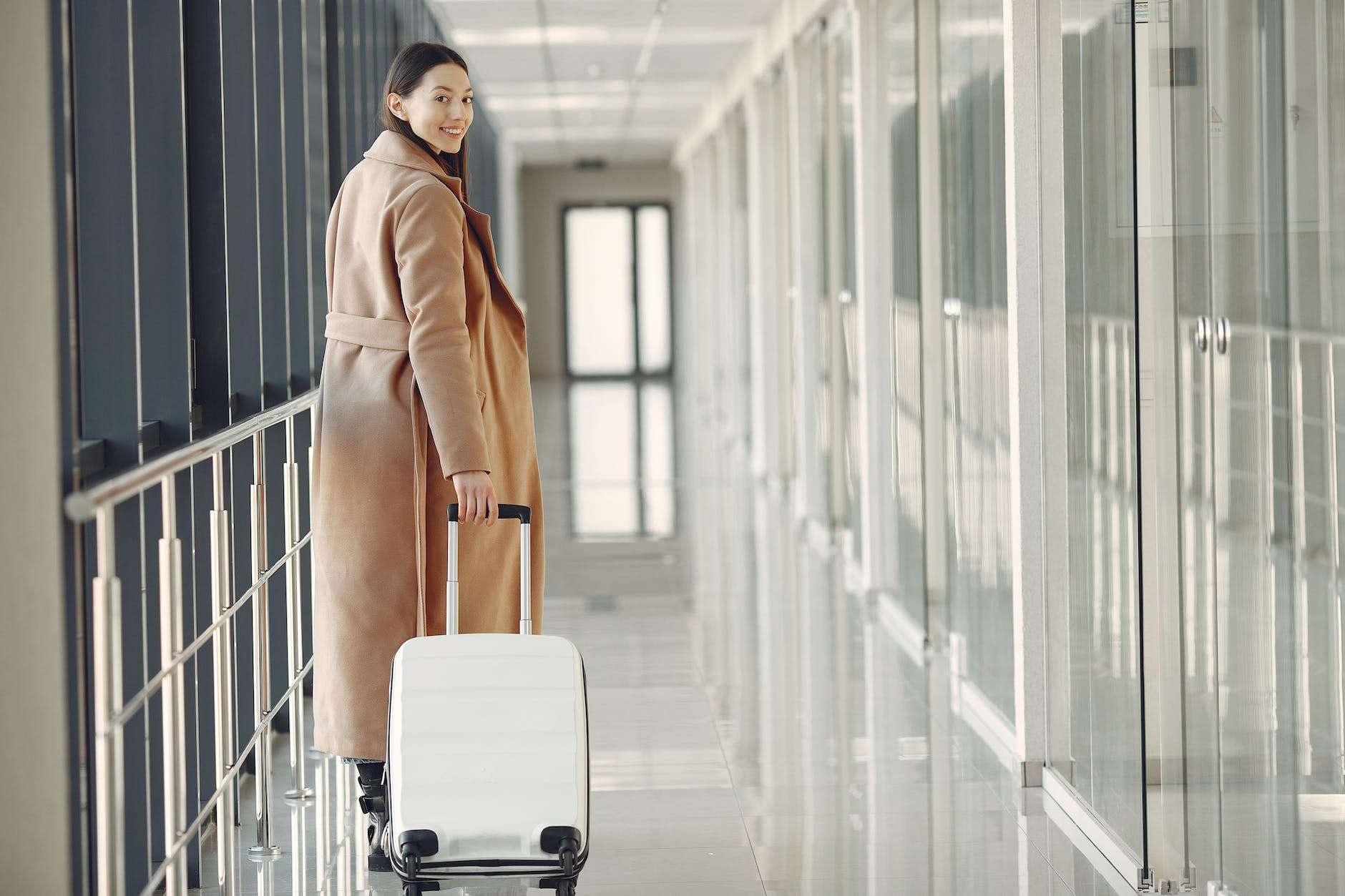 stylish happy traveler with suitcase in airport hallway